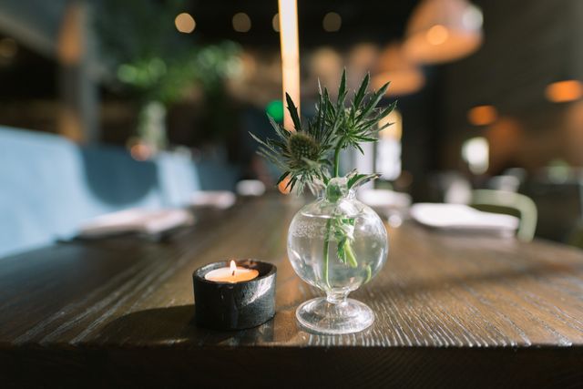 Intimate, cozy restaurant table featuring a lit candle and a small vase with a flower. Ideal for creating ambiance-themed projects, romantic dining promotions, and content emphasizing comfortable, serene dining experiences.