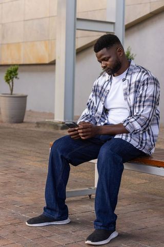 Casual man using smartphone while sitting on wooden bench in urban plaza