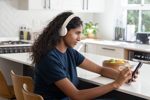 African american woman listening on headphones using smartphone at modern kitchen island