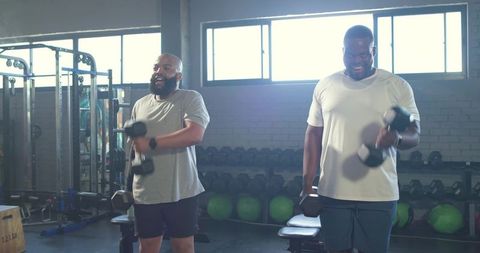 Two African American Men Lifting Dumbbells in Bright Gym for Partner Strength Training