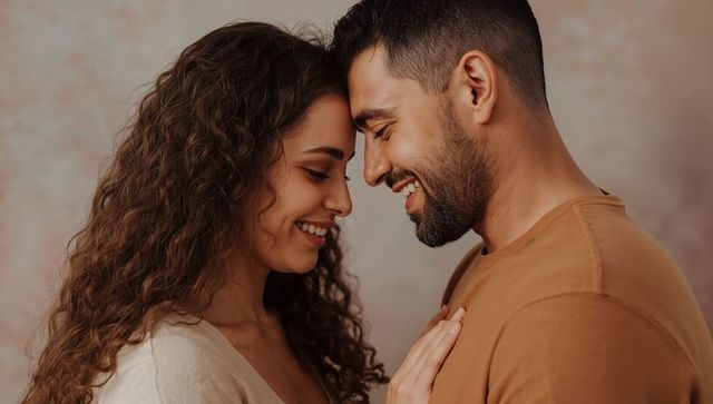 Intimate romantic couple touching foreheads smiling warmly in soft studio portrait