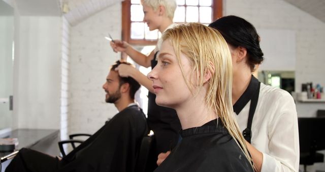 A young Caucasian woman is getting a haircut from a hairstylist in a salon, with copy space. Both the client and the stylist appear focused on the transformation taking place.