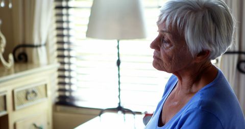 Elderly Woman Thoughtfully Sits on Bed