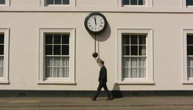 Walking commuter passing cream facade with pendulum clock and sash windows on sidewalk