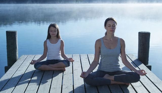 Mother and daughter meditating on misty lake dock at dawn for mindfulness and wellness