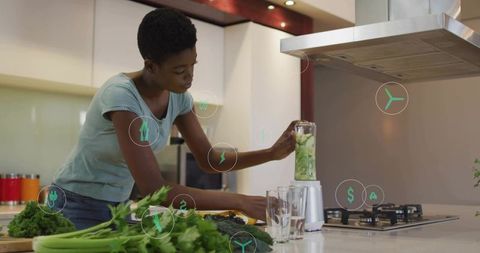 Black woman blending green smoothie at modern kitchen island with fresh greens