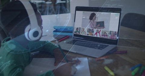 Young student wearing white headphones learning online and writing homework at home desk