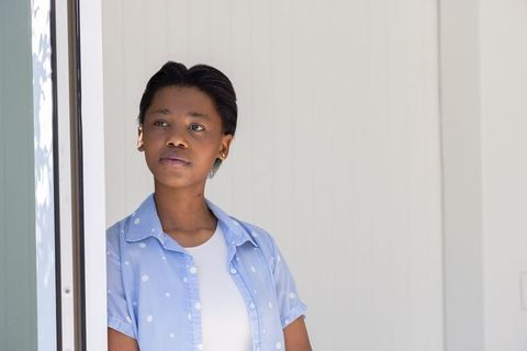 African teen leaning on door frame gazing outward minimal portrait soft light copy space