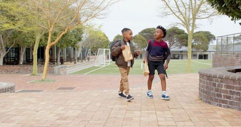 Diverse school boys walking and chatting on campus courtyard with backpacks and lunch bags
