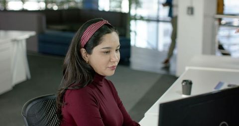 Hispanic professional woman typing at desk in modern coworking space, focused productivity