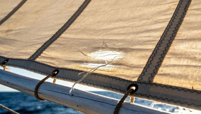 Backlit fraying sailcloth on sailboat boom with zigzag seams and grommets