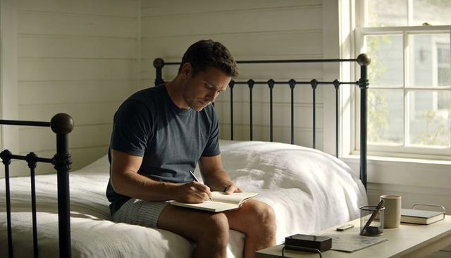 Middle-aged Man Journaling on Bed in Sunlit Rustic Bedroom Morning Routine