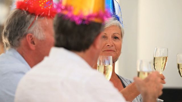 Mature friends celebrating a birthday together, wearing festive birthday hats, and toasting with champagne glasses. Perfect for use in content about senior social life, celebrations, family gatherings, and joyful moments.