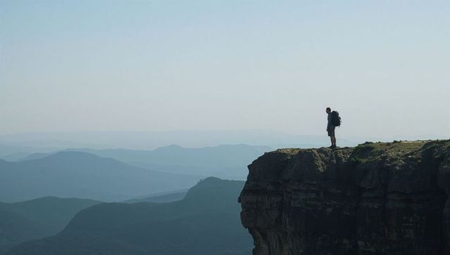 Hiker standing on cliff edge gazing over misty layered mountain ridges and valley