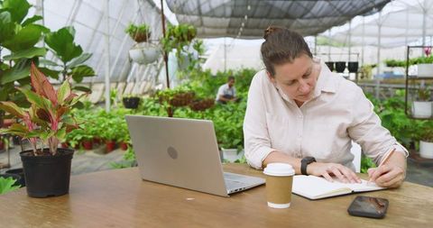 Woman Working and Taking Notes in Lush Greenhouse Environment