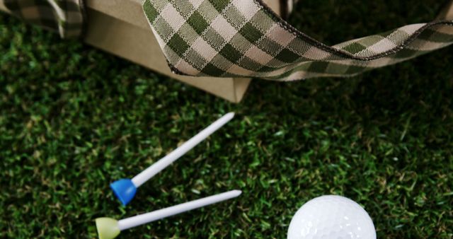 A golf ball and tees lie on the grass next to a patterned bag, with copy space. Capturing the essence of golf, the image suggests preparation for a game or practice session.