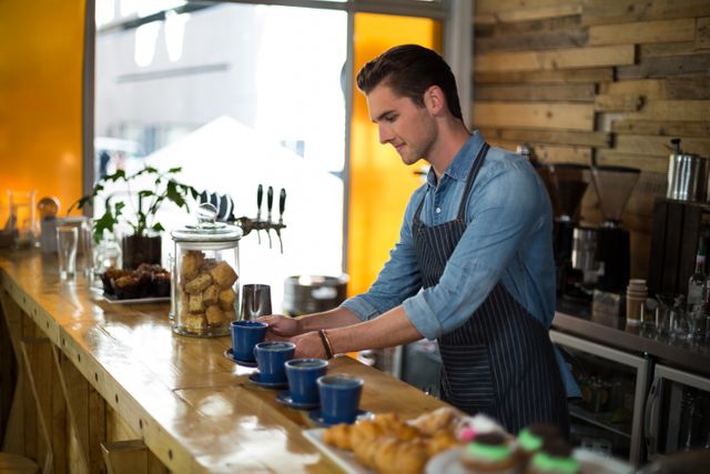 Waiter preparing cup of coffee at counter in cafÃ©