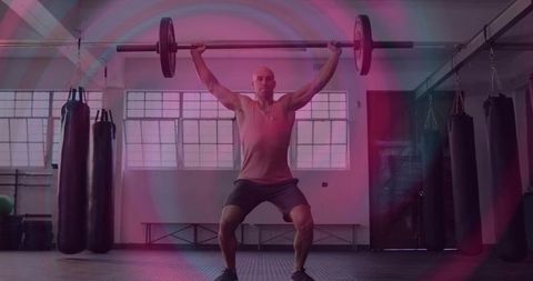 Mid-adult male performing overhead barbell press in gym emphasizing strength and focus