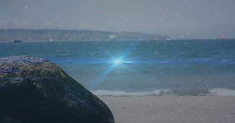 Mossy boulder sitting on sandy beach with blue lens flare and film grain overlay