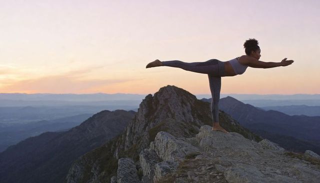 Sunset mountain yoga balance: woman holding single-leg warrior iii pose on rocky summit