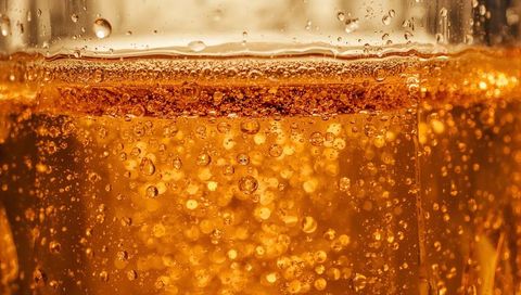 Macro bubble close-up: amber carbonated drink bubbling with golden fizz and foam