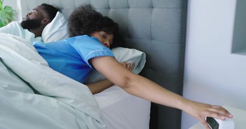 Black couple waking in minimalist bedroom woman reaching alarm clock morning routine