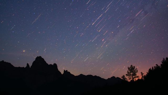Startrails streaking over jagged mountain ridge with Milky Way and silhouetted tree