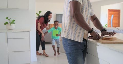 Dad slicing bread while son running and mom smiling in modern bright open-plan kitchen