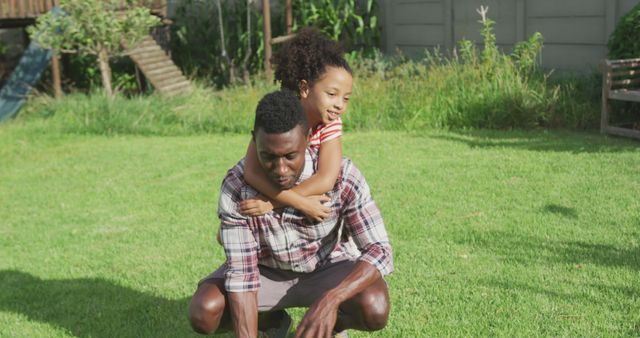 Smiling african american daughter hugging father in garden. Fatherhood, childhood, care, love, togetherness and summer.
