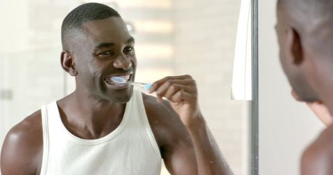 African-American Man Brushing Teeth in Bathroom Mirror Caring for Oral Hygiene Routine