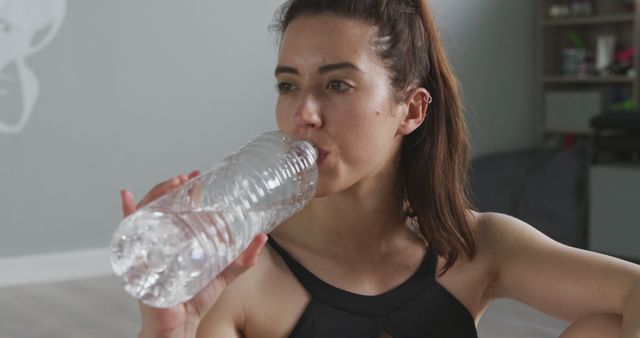 Biracial woman drinking water from bottle in gym - Download Free Stock Photos Pikwizard.com