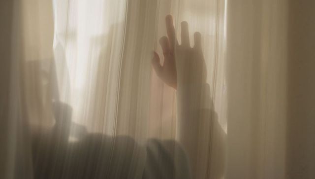 Pressing hand through sheer curtain casting soft silhouette and warm backlit glow