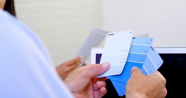 A person is selecting a shade from a palette of blue paint swatches, with copy space. Choosing the perfect color for a project can be crucial for achieving the desired aesthetic and mood.