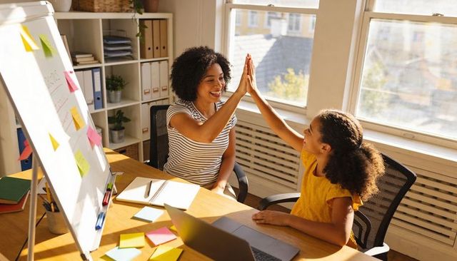 High-fiving woman and girl during home learning session with whiteboard and sticky notes