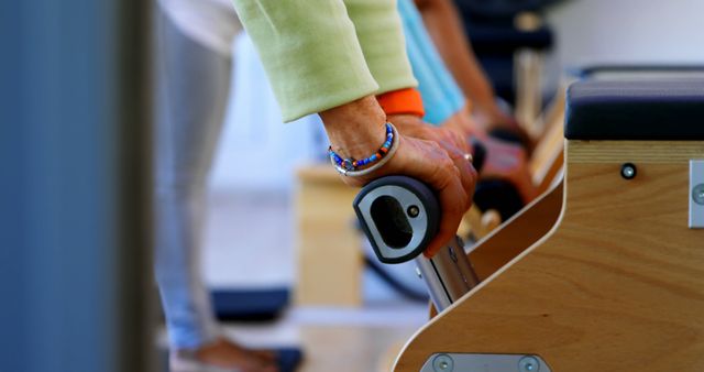 People engaged in Pilates workout in modern fitness studio. Close-up of hands using Pilates reformer equipment, highlighting fitness intensity and precision. Can be used for fitness advertisements, workout blogs, and manuals showcasing Pilates benefits.