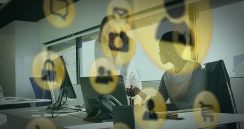 Coworkers collaborating and pointing at laptop with digital icons overlay in modern office