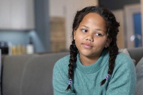 Young girl sitting on sofa looking thoughtful wearing teal sweater and braided hair