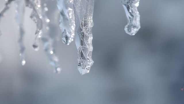 Glittering crystal icicle hanging from eave with faceted texture and frozen droplets