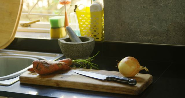 Freshly harvested carrots with dirt still on them and a whole onion resting on a wooden cutting board next to a knife. Sunlight illuminates the cozy, rustic kitchen with a mortar and pestle nearby. Perfect for themes around farm-to-table cooking, organic ingredients, and home-cooked meals.
