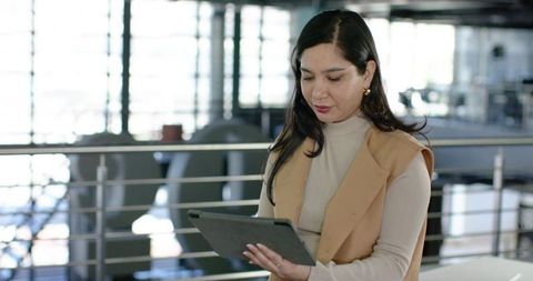 Professional woman holding tablet while leaning on railing in modern minimalist office