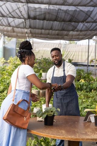 African american vendor processing card payment from customer at greenhouse plant nursery