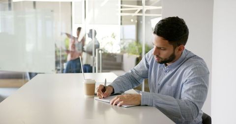 Focused Businessman Writing in Notebook at Modern Office Desk