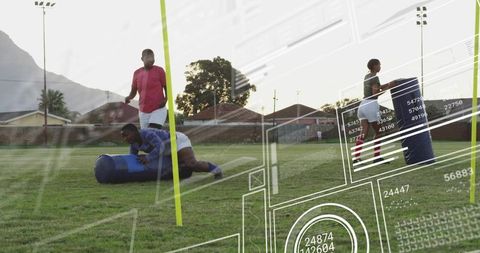 Girls rugby team training with blue tackle bag and yellow poles on community field at sunset