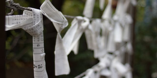 The image showcases Japanese omikuji fortune papers tied to a string, typically found at Shinto shrines. These papers represent people's wishes or fortunes and are tied to the shrine's designated area after being drawn. Perfect for use in articles or publications about Japanese traditions, spirituality, cultural activities, religious practices, and the intricate beauty of traditional customs. Can also be used in travel blog posts or educational material concerning cultural heritage and spiritual practices.
