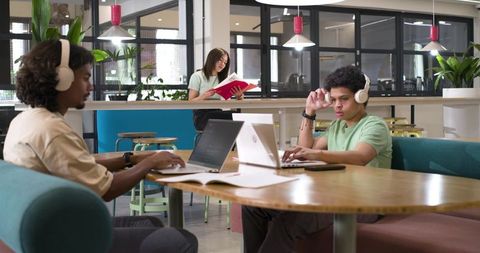 African American Professionals Working with Laptops and Headphones in Modern Coworking Space