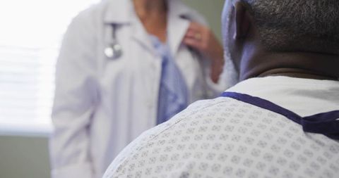 Doctor consulting senior patient wearing hospital gown during clinical examination with stethoscope