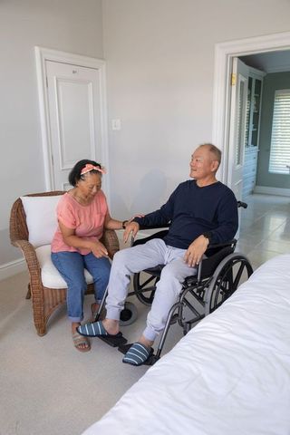 Senior asian couple sharing tender support woman holding man's hand by wheelchair