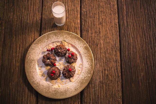 Christmas cookies arranged on a golden plate with powdered sugar, red berries, and almond flakes, placed on a rustic wooden table accompanied by a glass of milk. Suitable for holiday recipes, festive baking blogs, Christmas decorations, or holiday greeting cards.