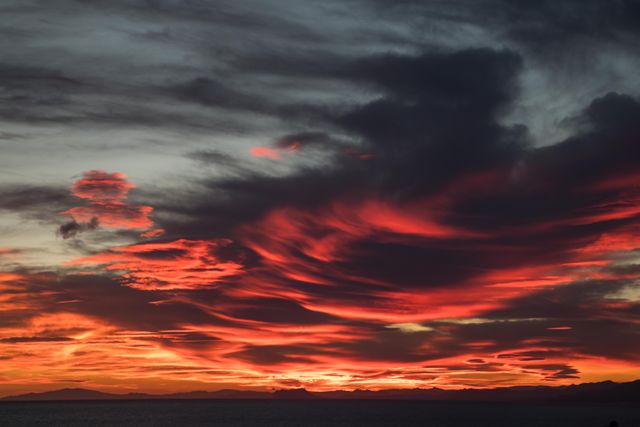 This image can be used for backgrounds in presentations, blog posts about nature or travel, and inspirational quotes. It captures a dramatic sunset with striking red and orange clouds over the horizon, showcasing the tranquil and captivating beauty of the evening sky.
