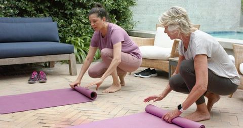 Senior women rolling out yoga mats on backyard patio beside pool